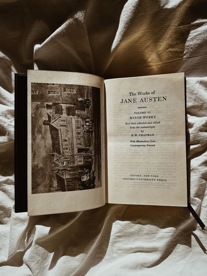 An open Jane Austen book on bed sheets, bathed in warm sunlight creating dramatic shadows.
